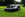 EGO AURA-R2 robotic lawn mower on a grassy lawn with trees in the background